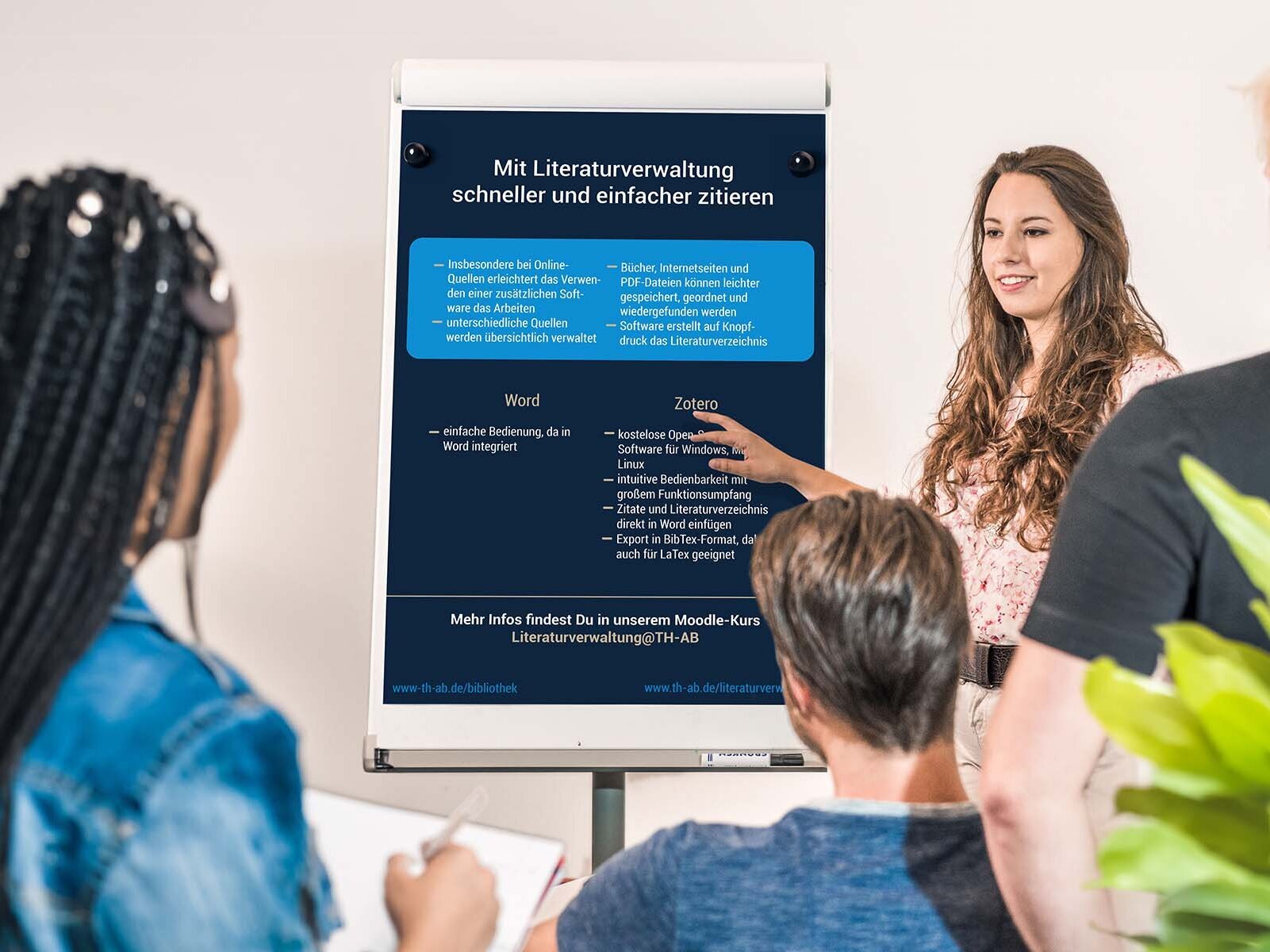 Drei Studierende hören einer Studierende, Referentin, Professorin, Dozentin zu, zeigt auf Flipchart mit Infos zum Zitieren