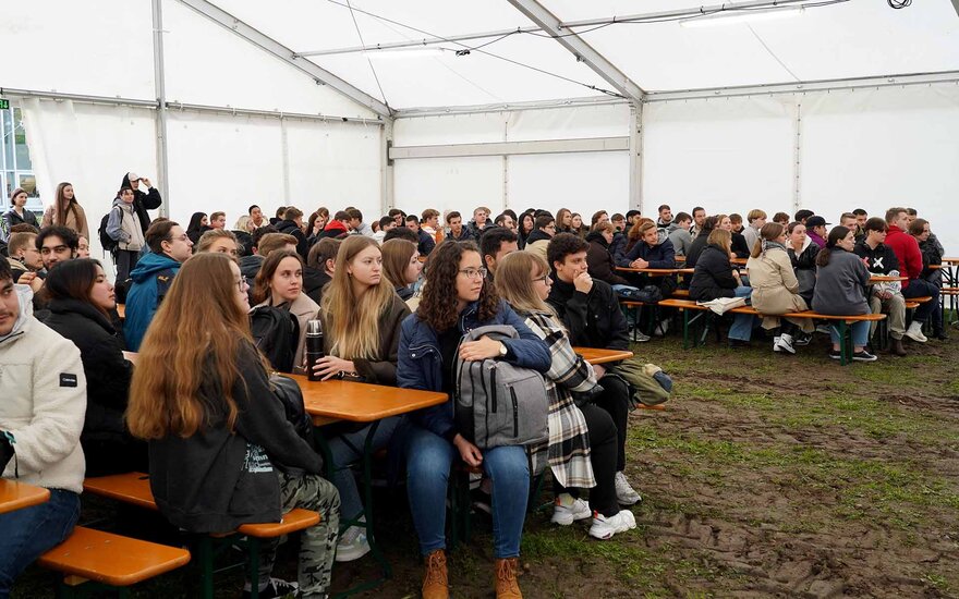 Studierende sitzen in einem Zelt auf Bänken