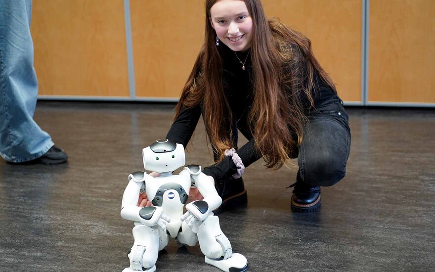 Ein lächelndes Mädchen hockt mit dem sitzenden Roboter auf dem Boden