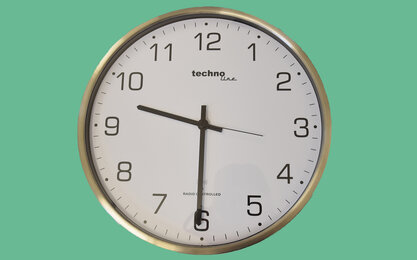 Silberne runde Uhr mit weißen Ziffernblatt und schwarzen Zeichen auf türkis grünem Hintergrund zeigt neun Uhr dreißig