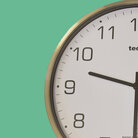 Runde Holzuhr mit weißen Ziffernblatt und Holzzeigern auf hellblauem Hintergrund