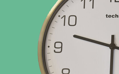 Runde Holzuhr mit weißen Ziffernblatt und Holzzeigern auf hellblauem Hintergrund