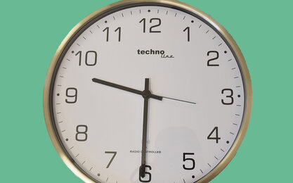 Silberne runde Uhr mit weißen Ziffernblatt und schwarzen Zeichen auf türkis grünem Hintergrund zeigt neun Uhr dreißig