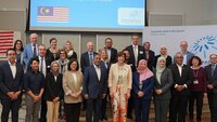 Mitglieder der Delegation aus Malaysia und Mitglieder der TH Aschaffenburg stehen als Gruppe in der Aula vor einer hellblauen Leinwand mit einem englischen Willkommensgruß, der malaysischen Flagge und dem TH-Logo darauf