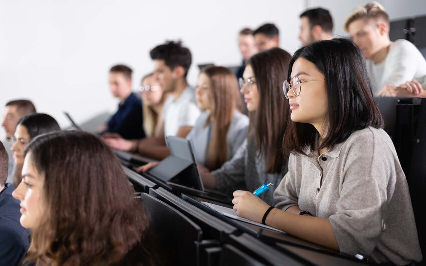 Studierende sitzen im Hörsaal, hören aufmerksam zu und schreiben mit.
