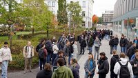 Eine große Gruppe neuer Studierender läuft zwischen zwei Gebäuden über den Campus der Hochschule