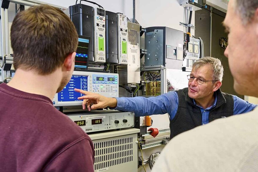 Ein Professor erklärt seinen Mitarbeiterin elektrische Spannungen am Oszilloskop.