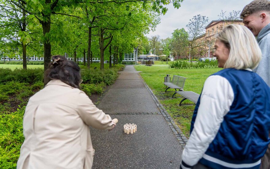 Drei Menschen spielen auf dem Campus ein Spiel.