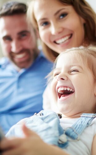 Familie Mann Frau zwei Kinder lachend auf Sofa sitzend