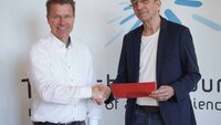Zwei Männer stehen nebeneinander und reichen sich lächelnd die Hand.