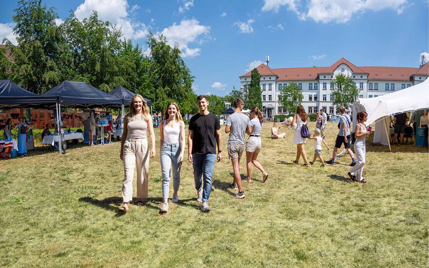 Besucherinnen und Besucher beim Open Campus an der Technischen Hochschule Aschaffenburg auf der Campuswiese mit Infoständen und dem weißen Gebäude der Fakultät Wirtschaft und Recht im Hintergrund