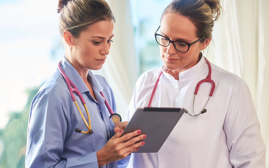 Zwei Frauen in Arbeitskleidung lesen sich eine Krankenakte durch.