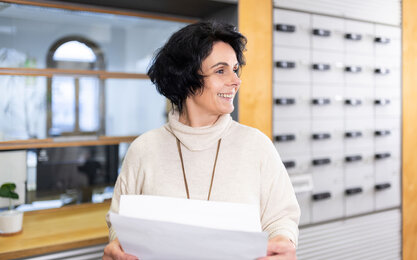 Frau steht vor Postfächern mit Papier in der Hand.