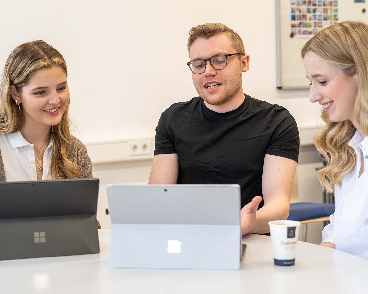 Luisa und zwei ihrer Kommilitonen sitzen vor zwei Laptops und unterhalten sich dabei lachend.