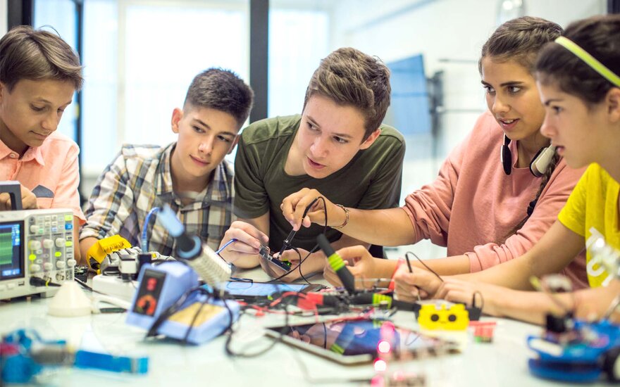 Fünf Jugendliche experimentieren zusammen an einem Roboterprojekt. Arbeitstisch voller verschiedener Objekte, die für die Aufzeichnung elektrischer Stromkreise benötigt werden.