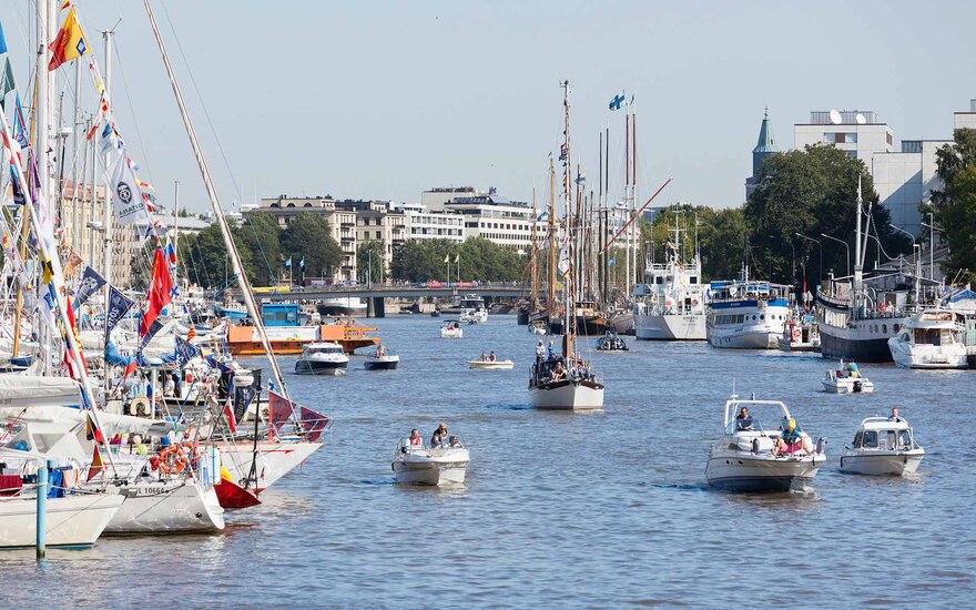 Segelboote auf dem Wasser an einem Hafen. Im Hintergrund ist eine Stadt. 