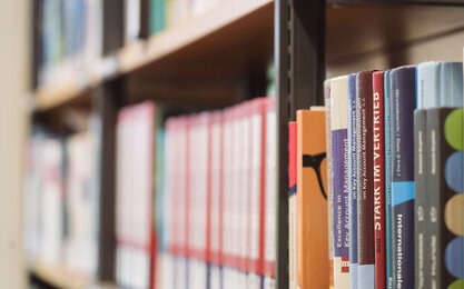 Verschiedenfarbige Bücher stehen in einem Regal.