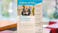 Einige Exemplare des aktuellen Hochschulmagazin "Campus aktuell" in einem transparenten Zeitschriftenständer vor einem Fenstser