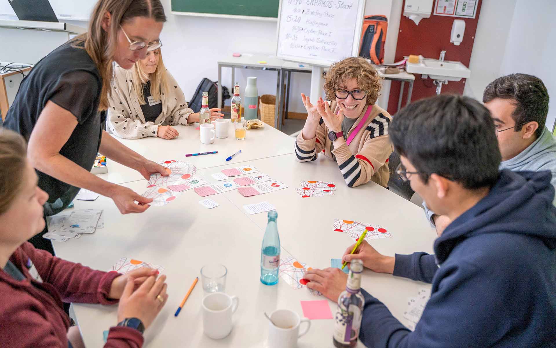 Teilnehmende der Kick-off-Veranstaltung sitzen an einem Tisch, diskutieren und notieren ihre Arbeitsergebnisse auf bunten Zetteln