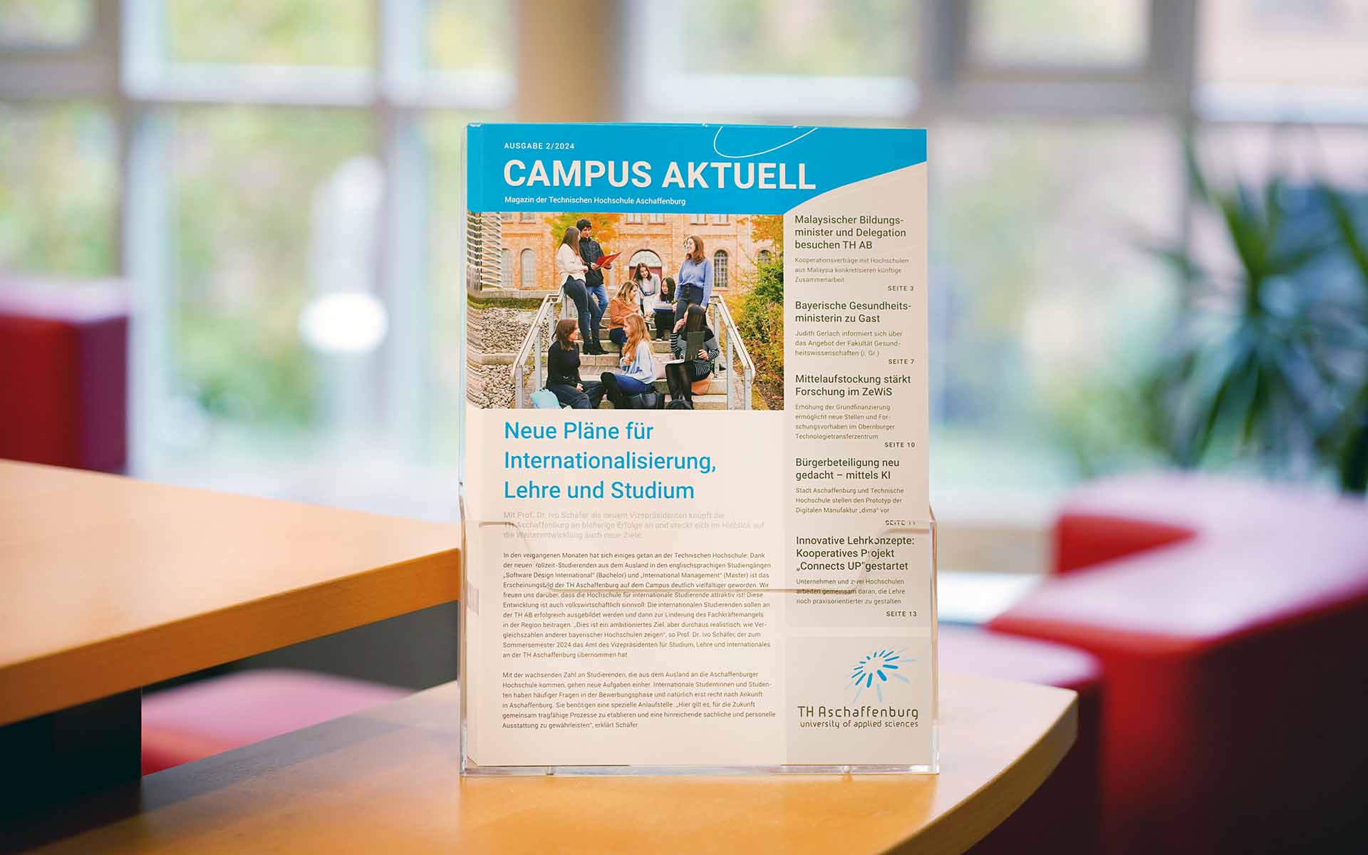 Einige Exemplare des aktuellen Hochschulmagazin "Campus aktuell" in einem transparenten Zeitschriftenständer vor einem Fenstser