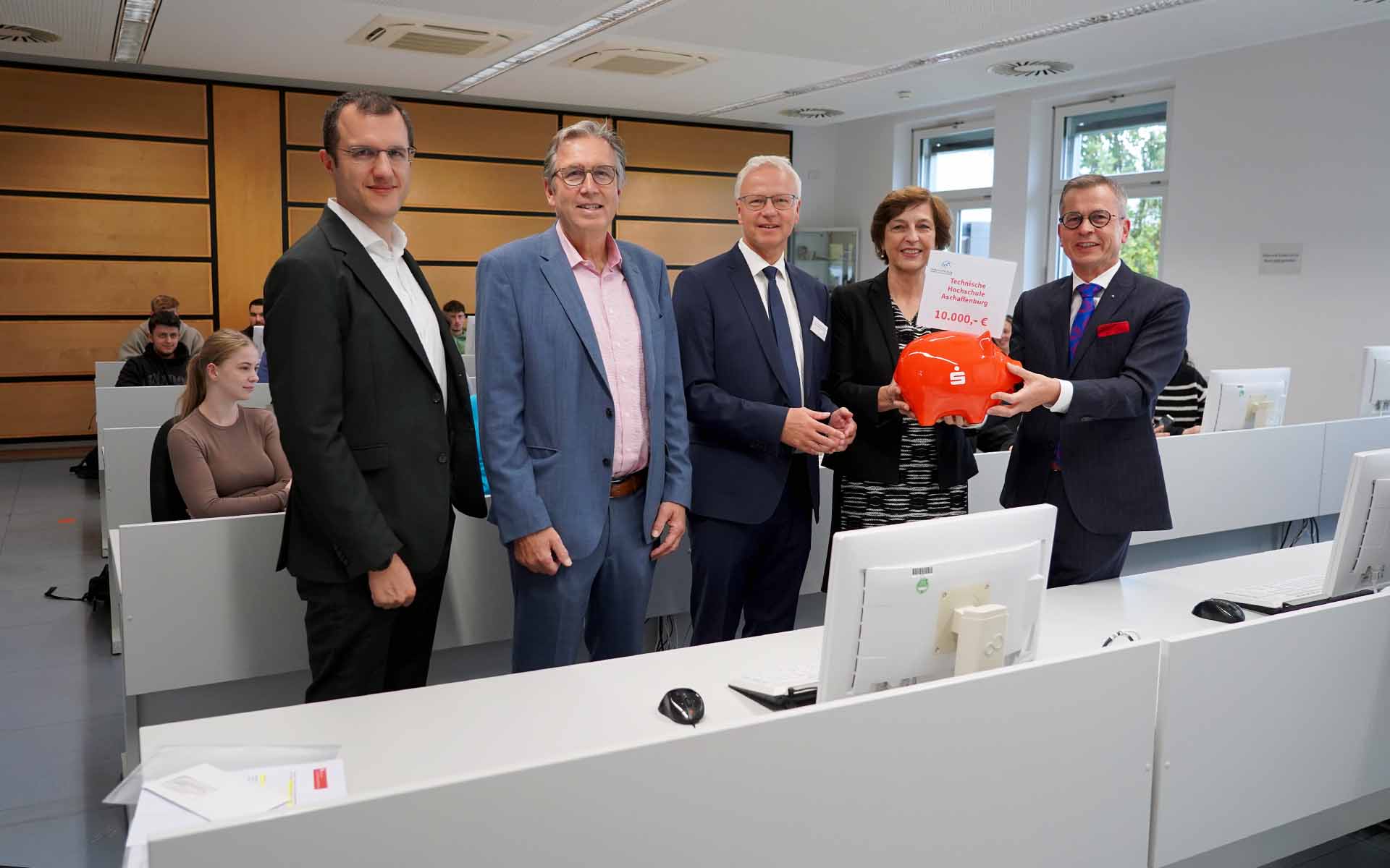 Der Vorstandsvorsitzende der Sparkasse überreicht der TH-Präsidentin sympolisch ein rotes Sparschwein mit einem Schild mit der Spendensumme, neben ihr die Professoren Rötzel und Pasckert und der Aschaffenburger Oberbürgermeister